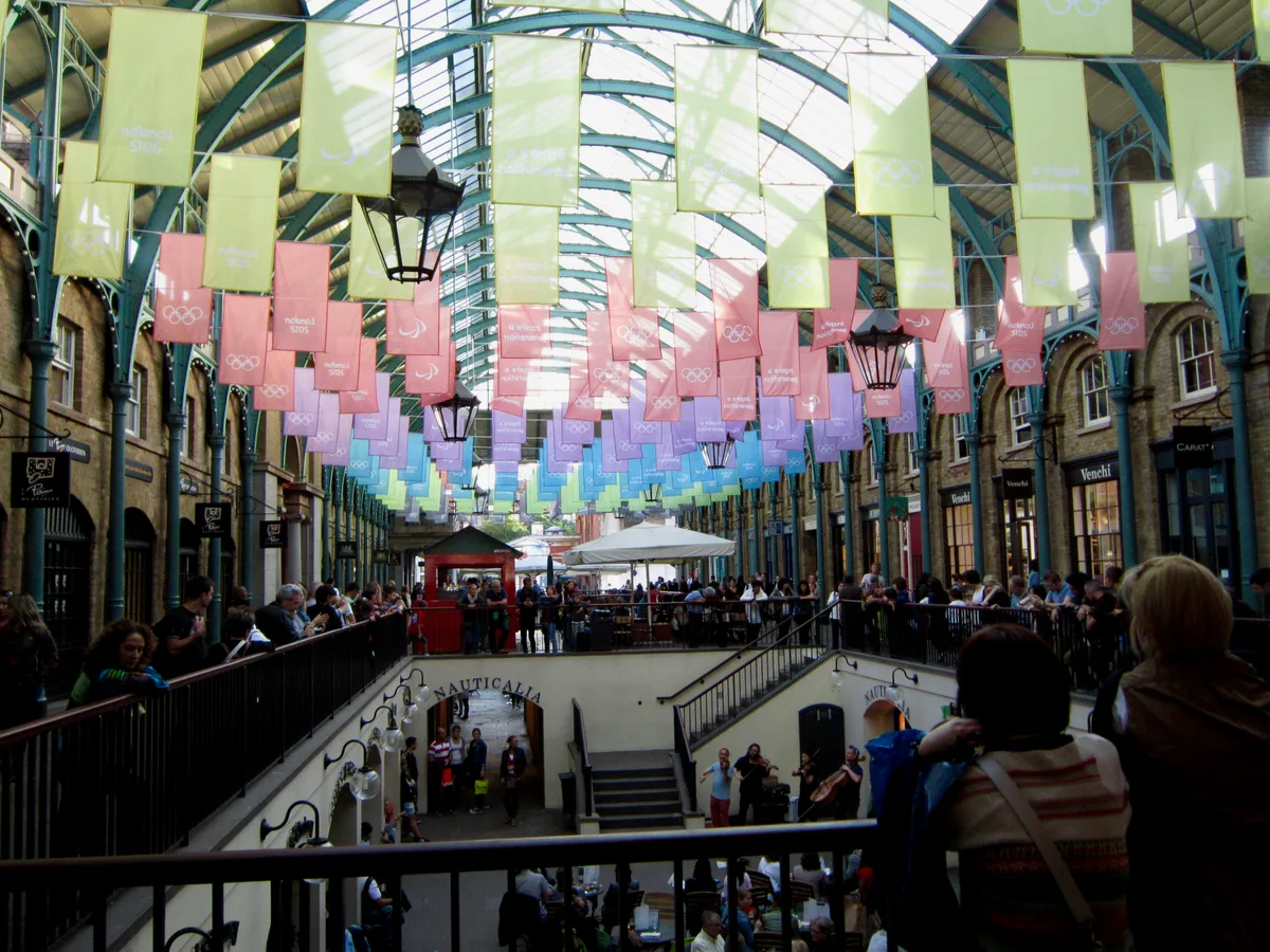 De victoriaanse overdekte markthal van Covent Garden in Londen met kunstenaars op de Piazza en mensen die rondkijken