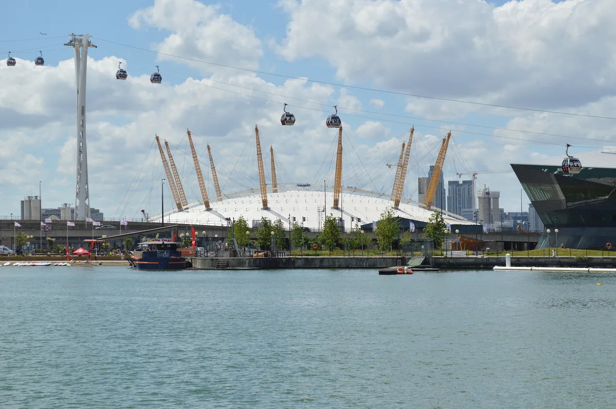 Mensen lopen over het witte koepeldak van The O2 Arena in Greenwich met de skyline van Canary Wharf op de achtergrond